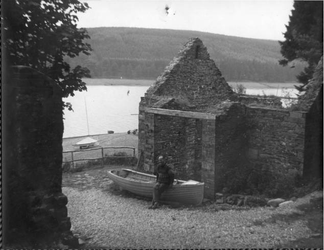 One of the early club members is pictured sitting on the gunwale of the boat alongside the building that later was converted to the clubhouse, with the reservoir in the background.